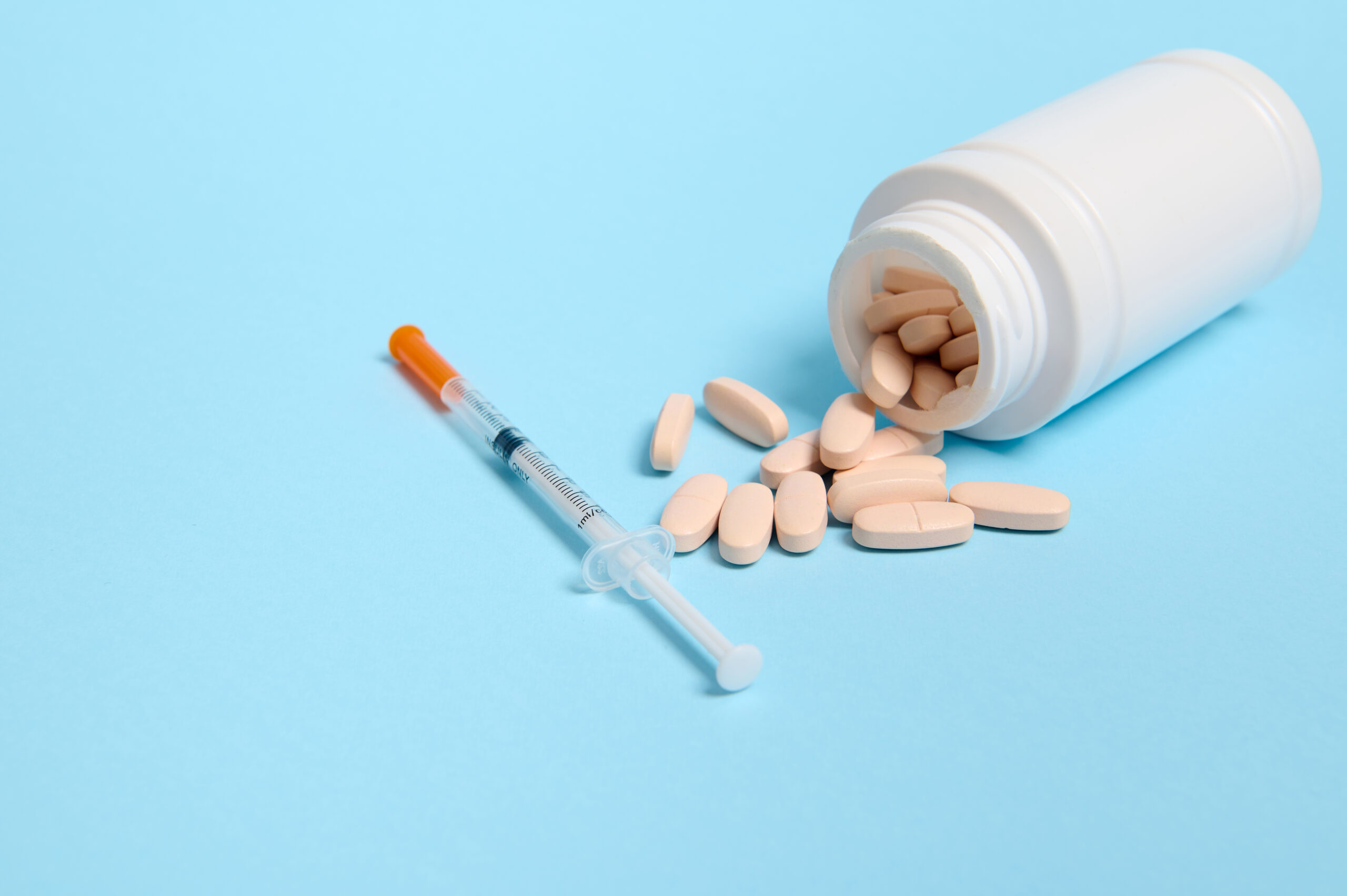 studio-shot-insulin-syringe-pharmaceutical-pills-scattered-from-white-medicament-container-blue-background |