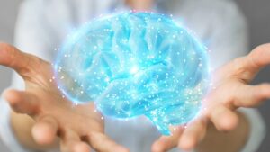 A person holding a glowing digital brain hologram with interconnected nodes and neural network lines, symbolizing technology, innovation, and neuroscience | Mind Brain Institute