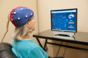 Woman wearing an EEG cap during a neurofeedback therapy session, using brain-training games to support treatment-resistant anxiety and cognitive improvement. | Mind Brain Institute