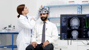 Doctor adjusting a QEEG headset on a patient during a neurofeedback session, with brain scan results displayed on a computer screen for neurological assessment. | Mind Brain Institute