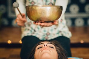 Sound bath therapy session with a Tibetan singing bowl held above a woman’s head, promoting relaxation, meditation, and holistic healing | Mind Brain Institute