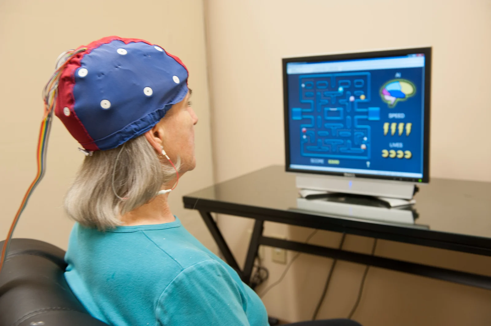 A woman can be seen sitting in front of a computer in which some readings can be seen attached with a head gear on the woman's head with some wires