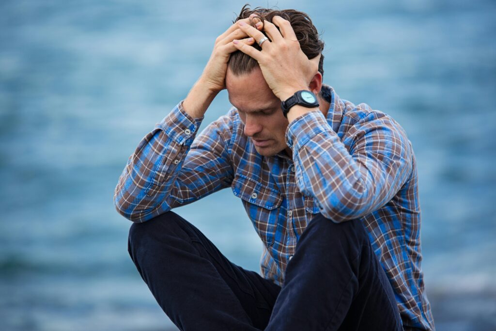 A man is sitting lost in thought with hands above his head struggling with his emotions