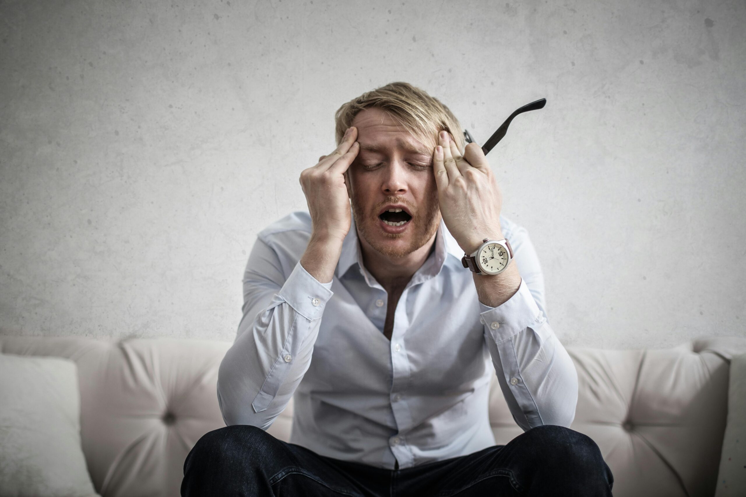 A man can be seen sitting on a sofa holding his head from both his hands and seems to be in lot of stress
