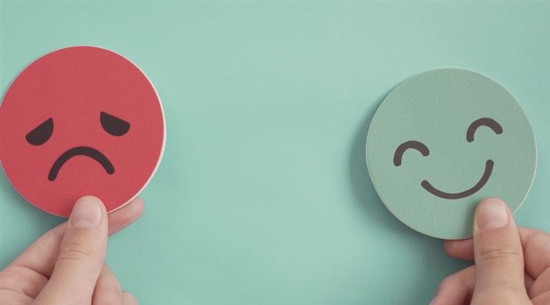 A person is holding two smileys happy and sad in both the hands