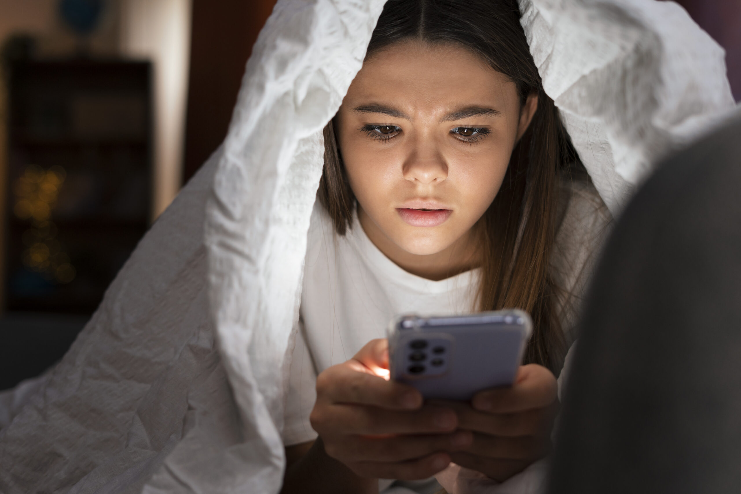 A young girl can be seen looking into her phone while covered in a quilt