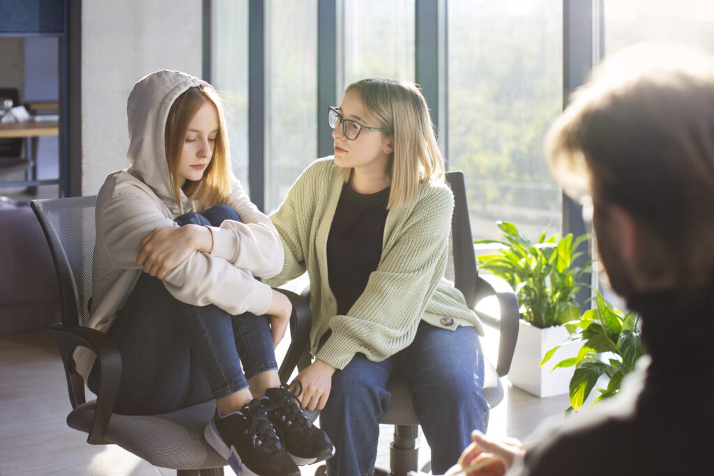 A woman can be seen consoling another woman with a man looking over both of them 