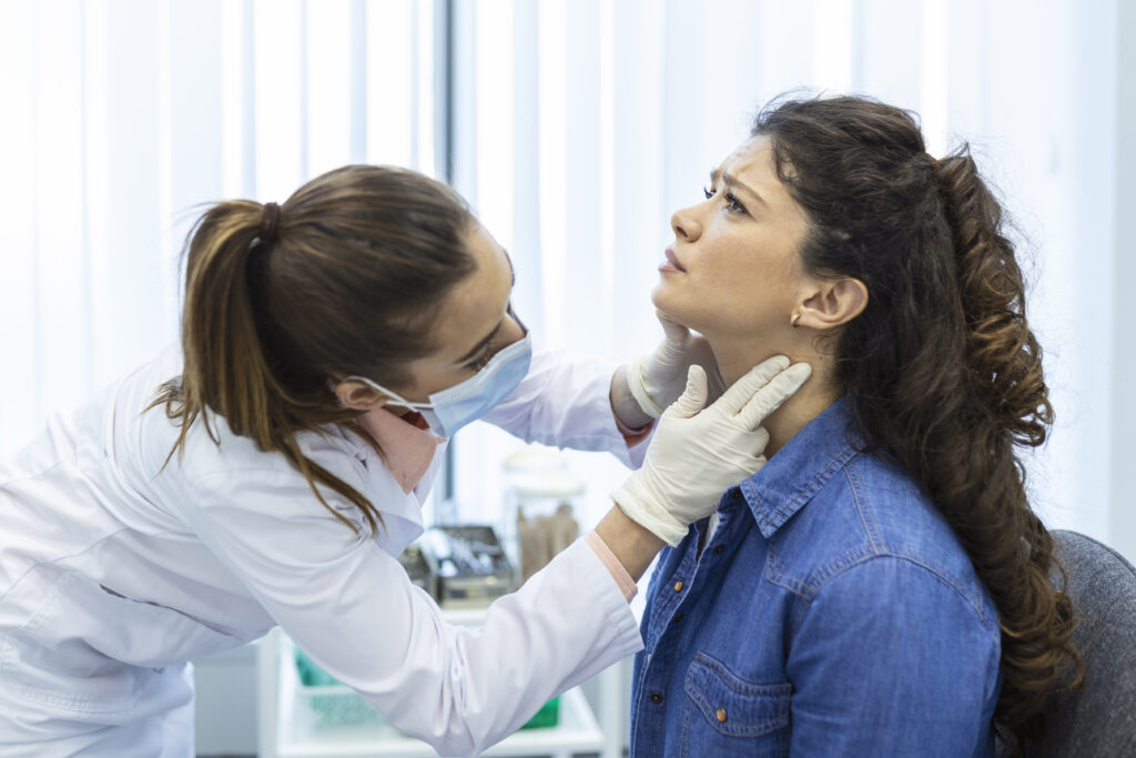 A female doctor can be seen inspecting the thyroid of another woman wearing blue shirt