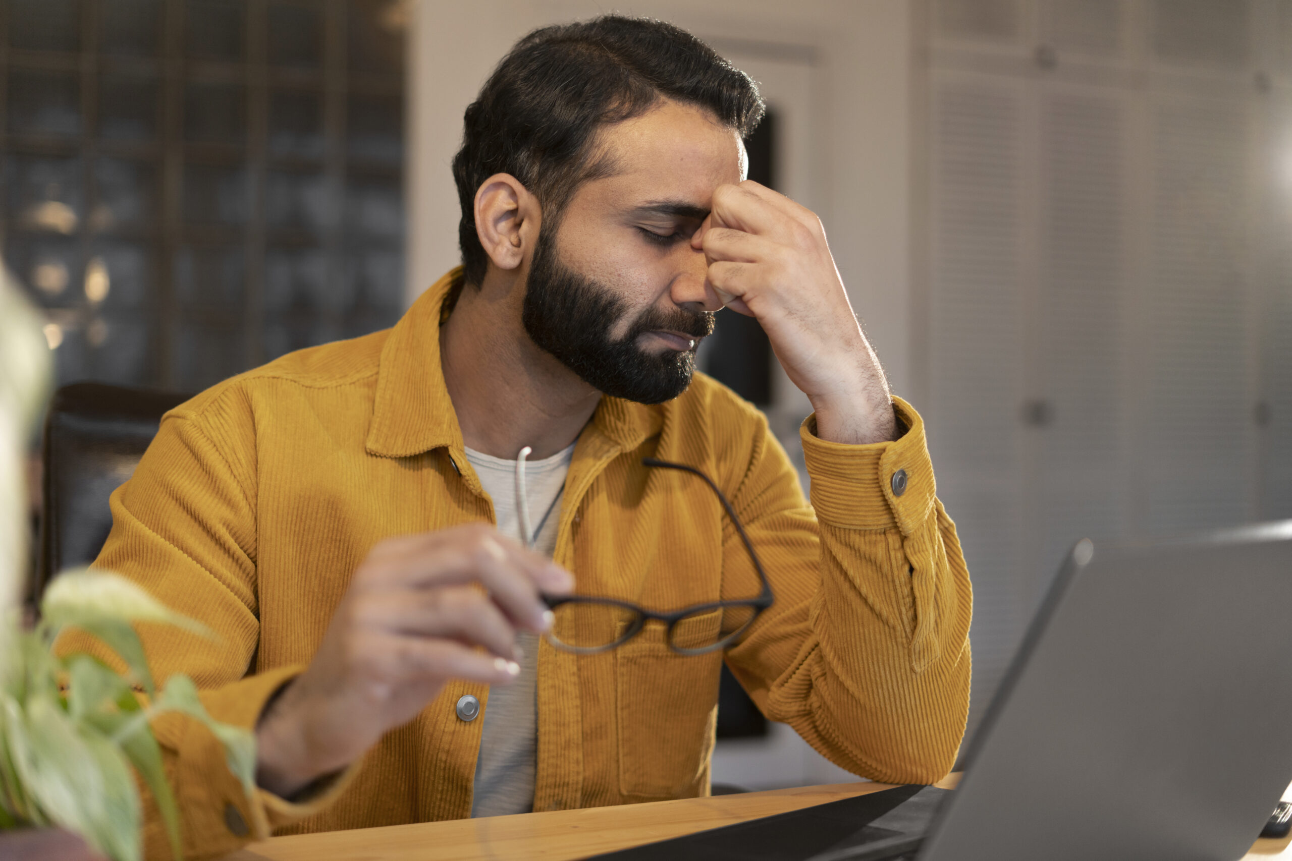 A man wearing a yellow jacket can be seen holding his face in a tense way holding his glasses from another hand