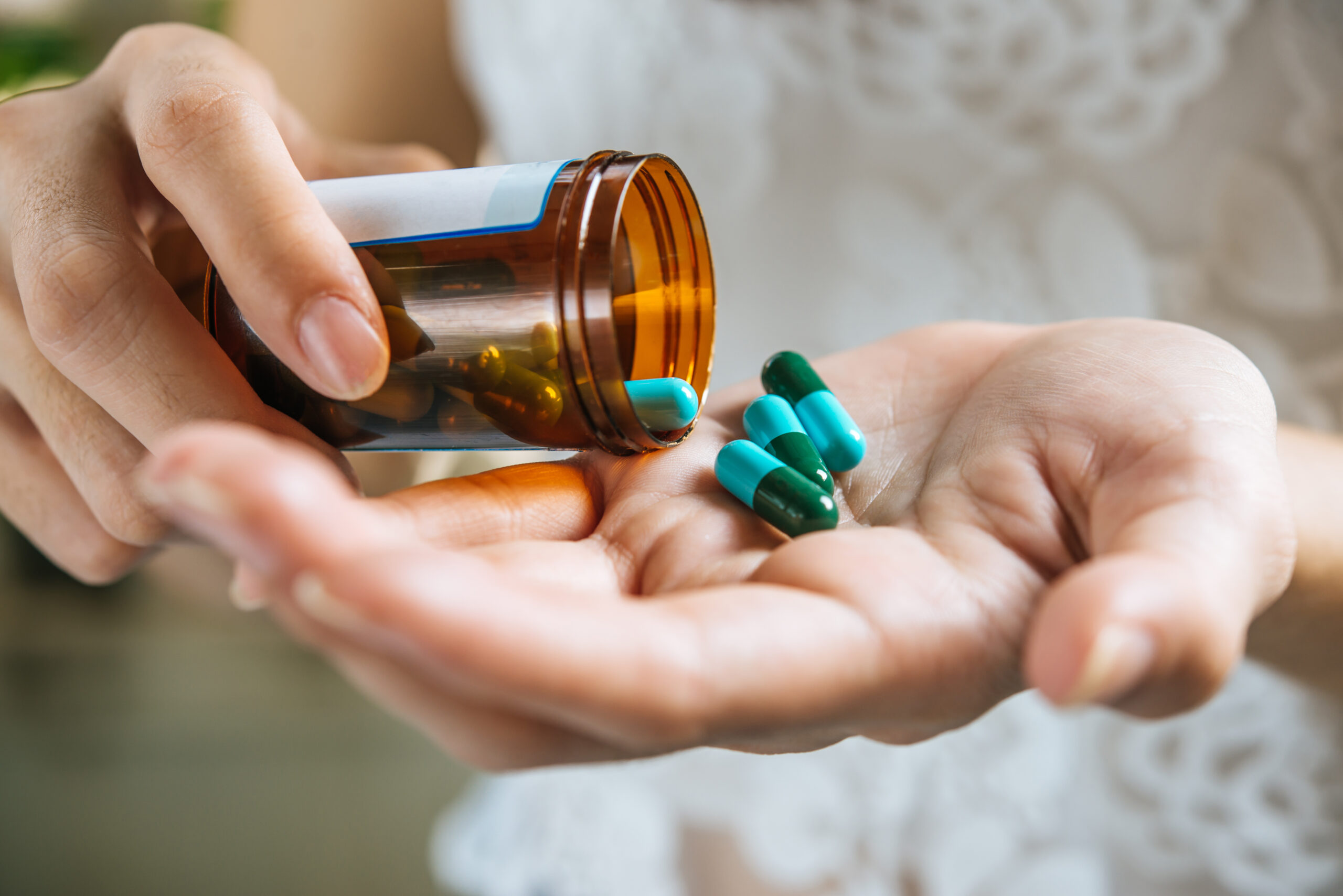 A woman's hand can be seen pouring out some medicinal tablets onto her hands