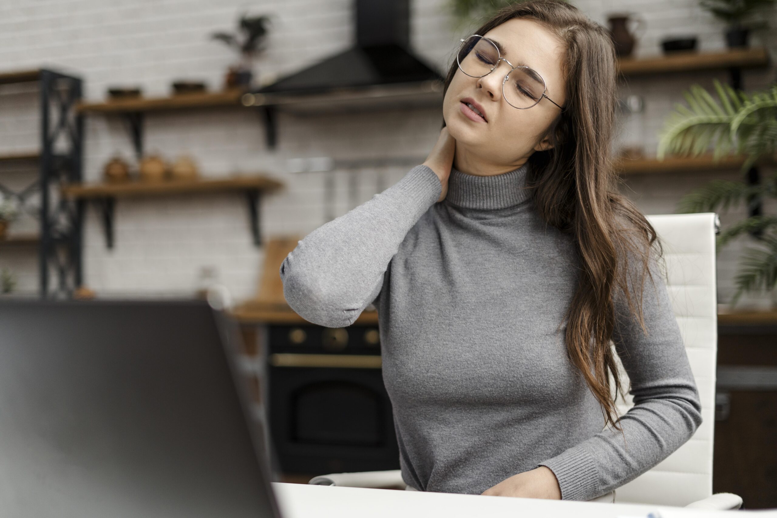 A young woman experiencing discomfort in her neck and can be seen sitting in a chair