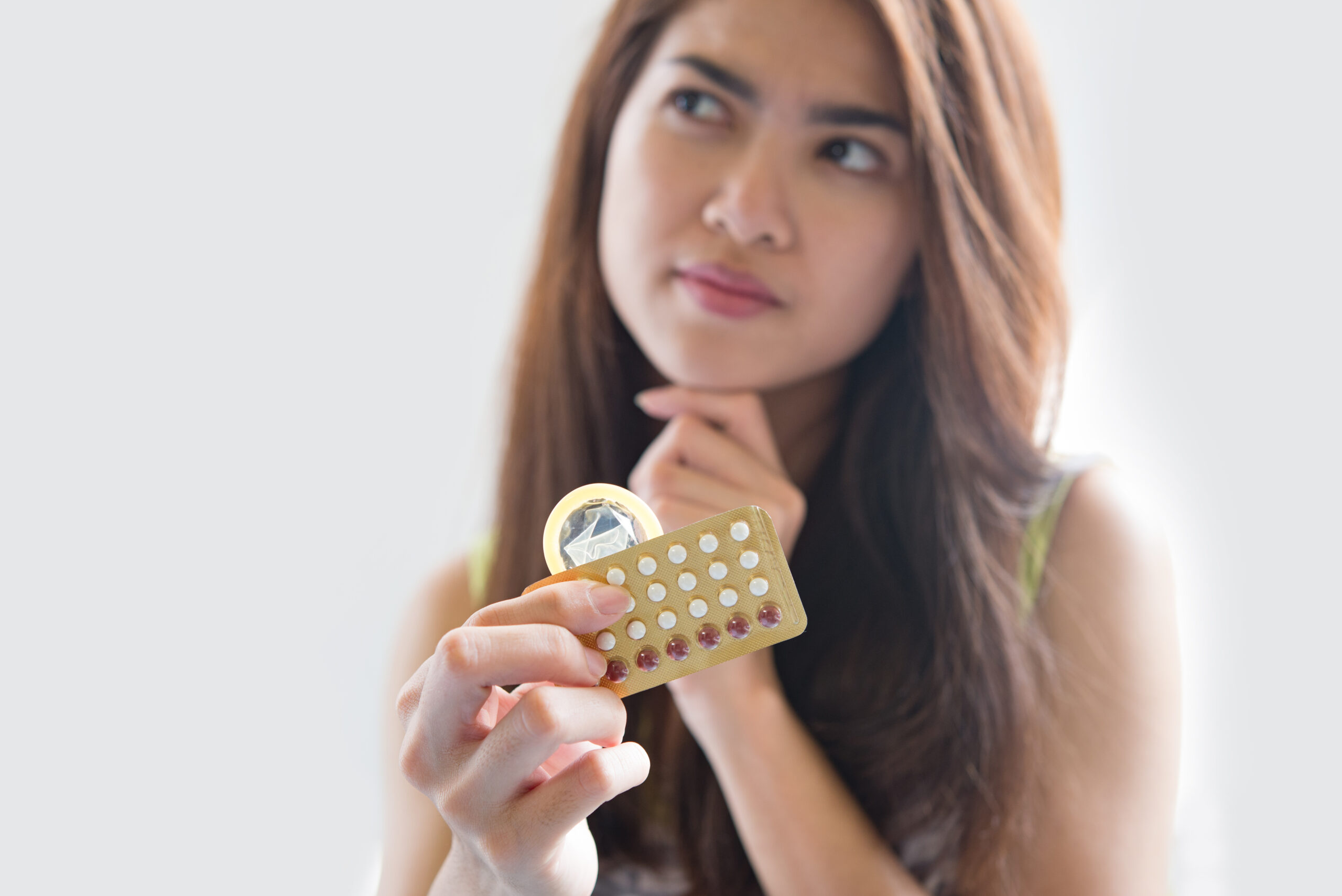 A young woman can be seen holding a contraceptive medicine and seems to be thinking something