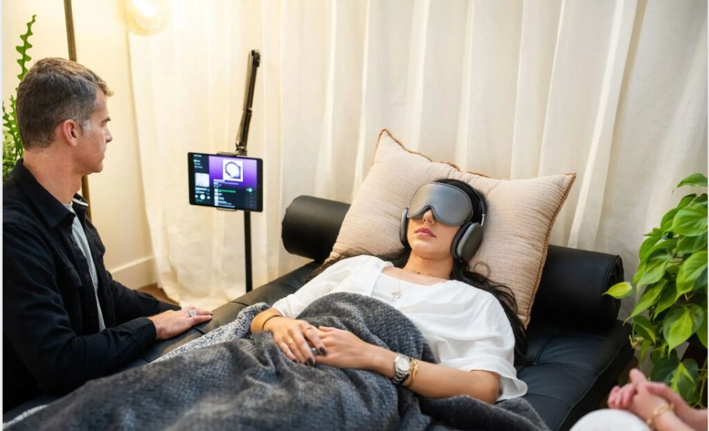 A woman can be seen lying on a bed with ketamine therapy going on with her and a man can be seen sitting beside her watching her medical readings