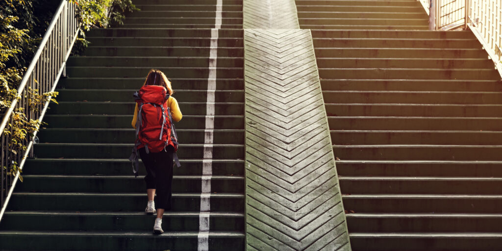 A young woman can be seen wearing a rucksack backpack and climbing stairs 