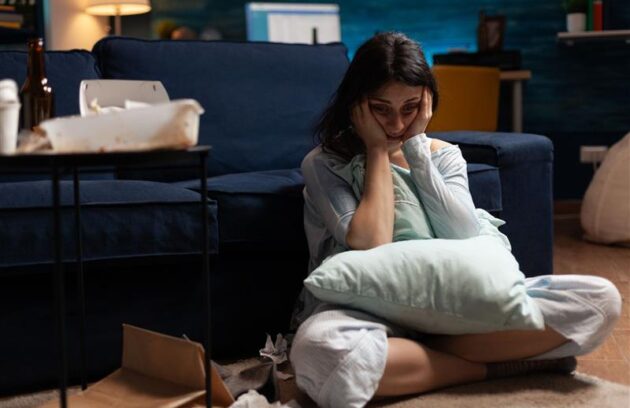 A woman can be seen sitting on her lap in the ground holding a pillow in her lap and holding her head in a tense manner as if pondering over something serious