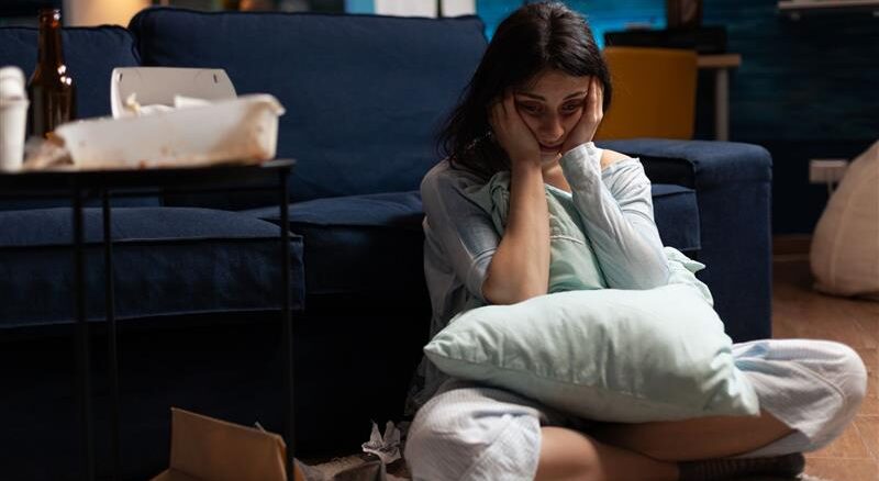 A woman can be seen sitting on her lap in the ground holding a pillow in her lap and holding her head in a tense manner as if pondering over something serious