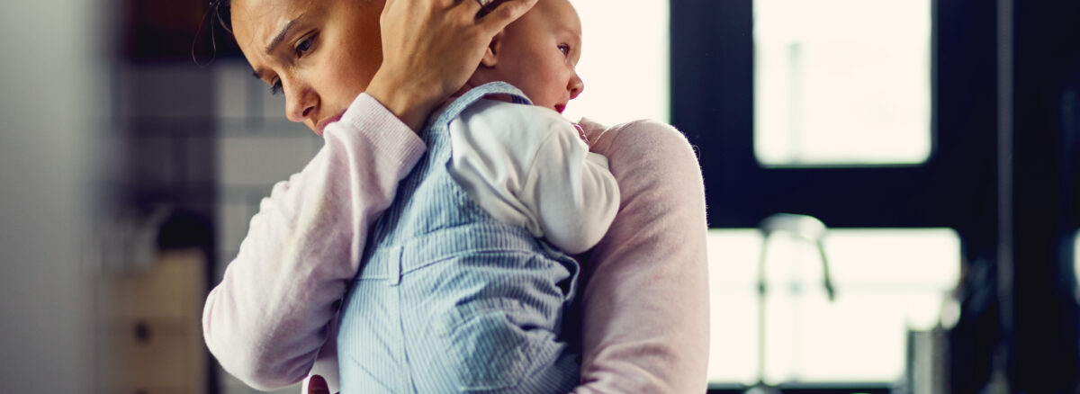A young mother can be seen comforting her crying baby in what appears to be a ktchen with a blurred background