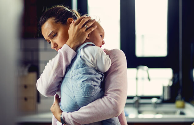 A young mother can be seen comforting her crying baby in what appears to be a ktchen with a blurred background