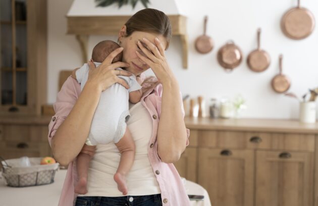 A young mother can be seen holding her baby and looking tense as she holds her head from another hand