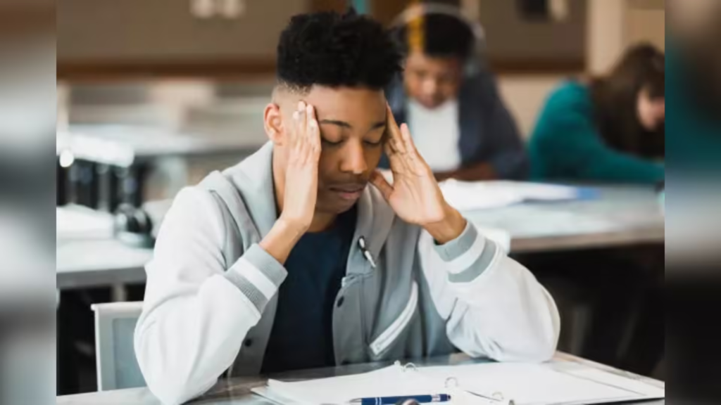 A young man can be seen holding his head in a tense manner while sitting in a classroom
