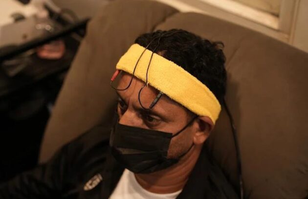 A man sitting in a tense manner wearing a TMS headset and looking worried