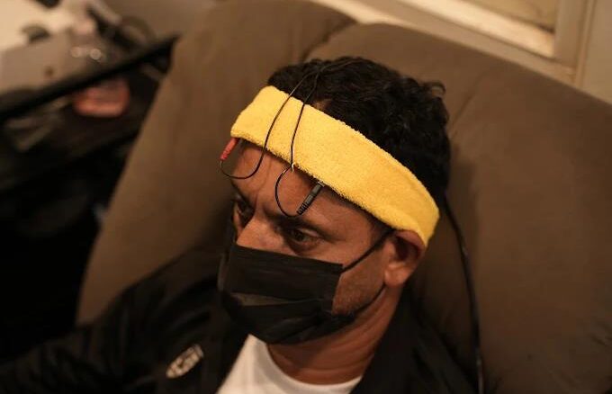 A man sitting in a tense manner wearing a TMS headset and looking worried